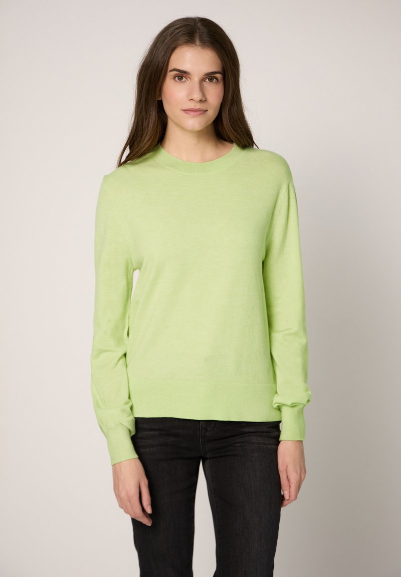 Maglione verde chiaro a maniche lunghe con collo rotondo e polsini a costine, realizzato in materiale morbido. Abbinato a jeans neri.