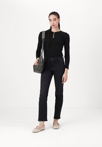 Fekete, hosszú ujjú ing elöl gombokkal, sötét farmernadrág, világos bézs lakások és szürke crossbody táska. Egyszerű háttér.