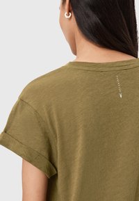 Olivgrünes T-Shirt mit umgeschlagenen Ärmeln, weicher Textur, rundem Ausschnitt und einem kleinen Logo auf der Rückseite in der Nähe der Schulter.