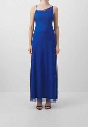 Femme portant une longue robe sans manches bleu roi avec un détail en tissu transparent au niveau du décolleté et de l'ourlet, associée à des talons ouverts noirs.