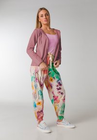 Ljusrosa zip-up jacka över en ljusrosa tank top; blommönstrade, löst sittande byxor med elastiska muddar; vita och pastellfärgade sneakers.