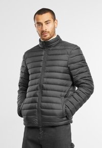 Sort pufferjakke med horisontal quiltet design, opretstående krave, lynlås foran og sidelommer. Glat, let skinnende tekstur.