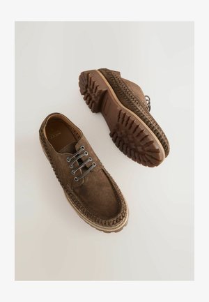 Pruunist nahast kingad tekstuuriga viimistlusega, millel on kaks metallist silma, paelad ja robustne tallalähedane tegumood. Kootud dekoratiivne ääris kaunistab servasid.