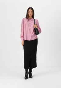 Camisa rosa de botões com mangas bufantes, combinada com uma saia preta com fenda e botas pretas até ao joelho. Bolsa preta transversal no ombro esquerdo.