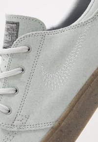 Baskets en daim gris clair avec logo swoosh blanc cousu, lacets blancs et semelle en caoutchouc translucide à motifs.