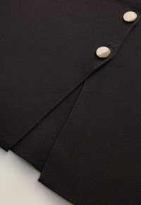 Tessuto nero testurizzato con una cucitura pulita e due bottoni a pressione argentati, che evidenziano un design minimalista e una costruzione robusta.