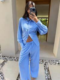 Conjunto de pijama azul riscado com camisa de botão de mangas longas e calças de perna larga, apresentando detalhes em pontos brancos e um corte descontraído.