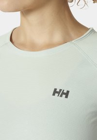 Světle zelená košile s krátkým rukávem vyrobená z texturované tkaniny, s kulatým výstřihem a černým logem na levé části hrudi.