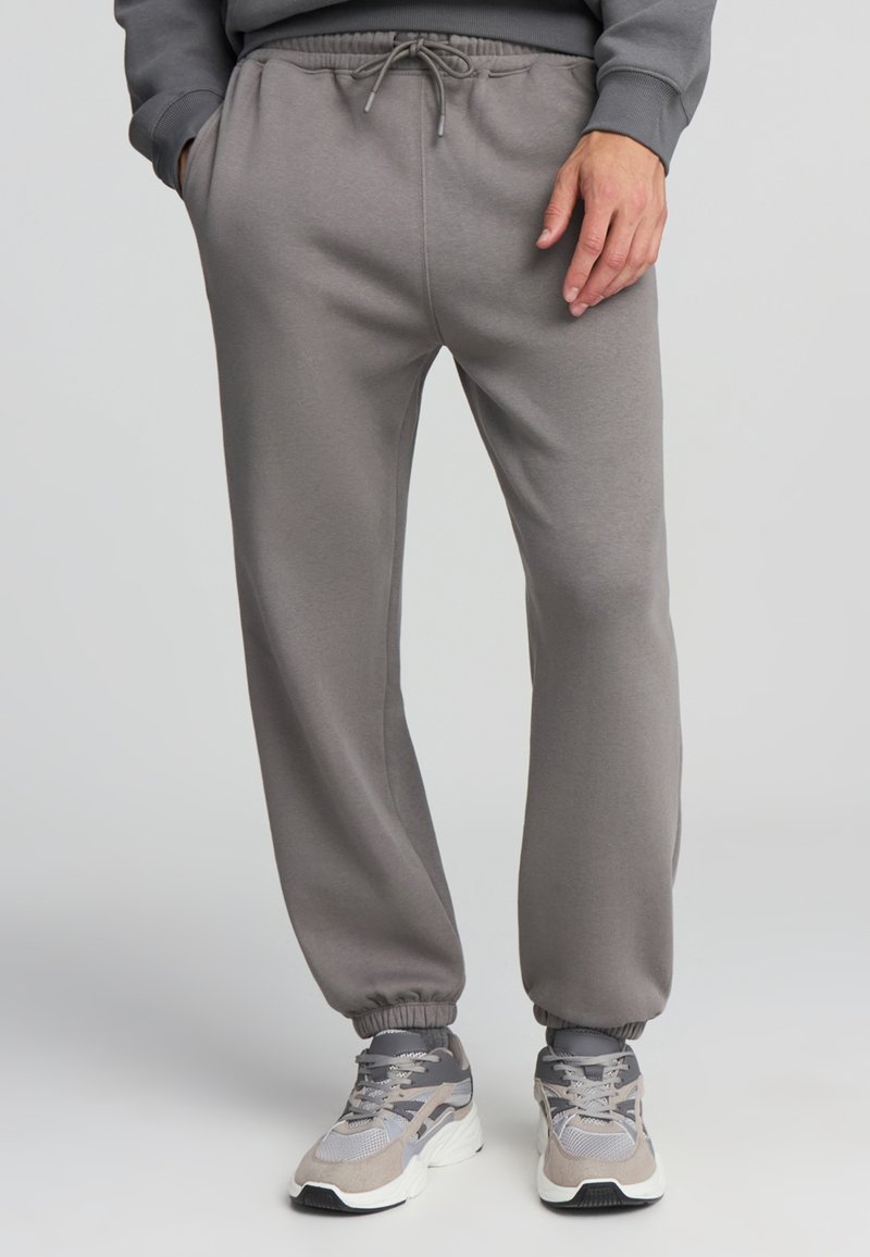 Szare spodnie dresowe z elastycznym pasem i mankietami, z bocznymi kieszeniami i sznurkiem do regulacji. Wykonane z miękkiego, gładkiego materiału.
