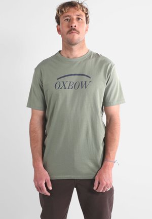 T-shirt en coton vert olive à manches courtes et col rond, présentant un graphique "OXBOW" en bleu foncé sur le devant. Conception unie au dos.