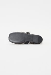 Tongs noires avec une semelle texturée et à motifs. Dotées d'une bride lisse et d'un logo en relief. Design léger et flexible.