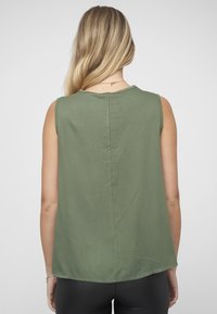 Ermeløs, olivengrønn topp med rund hals, myk tekstur og detaljert søm bak. Nederkanten er litt buet.