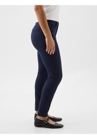 Pantalons ajustés bleu marine avec une texture lisse, dotés d'une taille mi-haute et de deux poches. Associés à des ballerines à brides noires.
