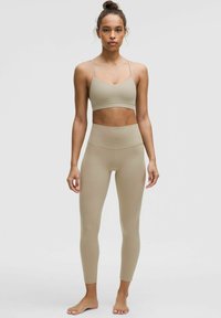 Svetlo béžová športová súprava obsahujúca priliehavú športovú podprsenku s tenkými ramienkami a legíny s vysokým pásom; hladká textúra a elastický materiál.