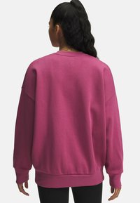 Przesadzony różowy sweatshirt z okrągłym dekoltem oraz ściągaczami na rękawach i u dołu. Miękka tkanina; bez widocznych wzorów, noszony z czarnymi spodniami.