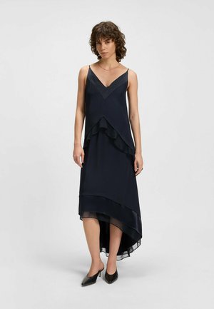 Navy sleeveless dress with a V-neck, layered design, and high-low hem. Smooth, flowing fabric with a transparent overlay at the hem.