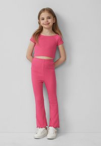 Roze geribde crop top en flared broekset met geschulpte zoomdetails, gecombineerd met witte sneakers met decoratieve accenten.