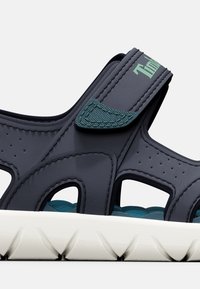 Sandali chunky di colore blu scuro con fori traspiranti, cinturini testurizzati e una suola bianca rigata. Presentano una chiusura regolabile in velcro.