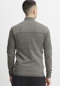 Grå strikket genser med høy krage, med horisontale teksturerte striper og ribbestrikkede mansjetter og bunn. Mykt, middels tykt materiale.