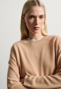 Maglione in cashmere beige con scollo a costine e dettagli sulle spalle. Morbido al tatto, vestibilità comoda e maniche lunghe.