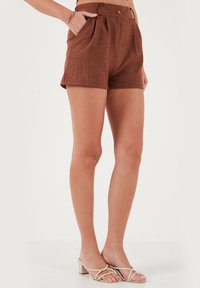 Shorts en lin marron au design ajusté, avec des plis à l'avant, une fermeture à bouton et des poches latérales. Texture lisse et longueur courte.