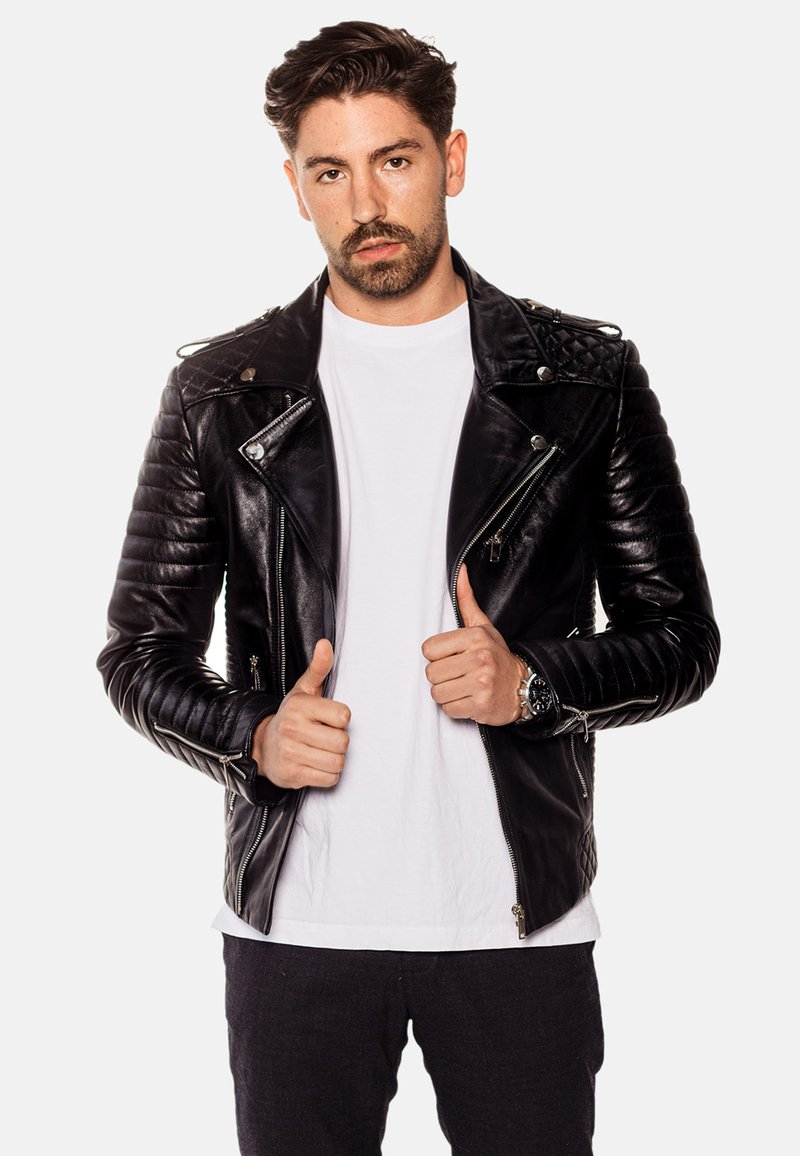 Svart läderbikerjacka med kviltade axlar, silverdragkedjor och en figurnära design. Buren över en vit t-shirt, visad med tummen upp.