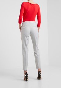 Top rojo de manga larga combinado con pantalones ajustados gris claro con rayas laterales. Sandalias negras de tacón con tachuelas doradas completan el conjunto.