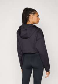 Cropped black hoodie with a hood, featuring a smooth texture and relaxed fit. Paired with black leggings, showing a clean seam design.