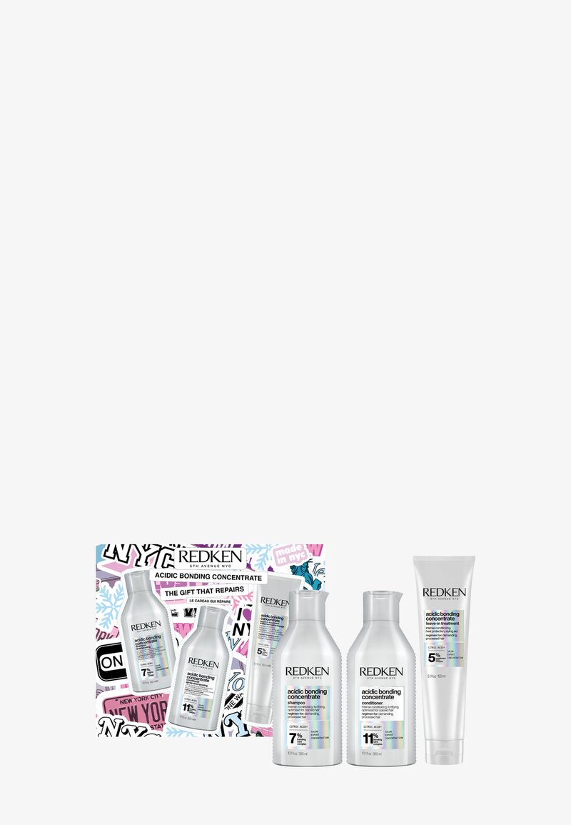 Redken presentask med fyra flaskor: silverfärgad cylindrisk schampo och balsam, krämfärgad leave-in behandling, och en låda med NYC-temat design.