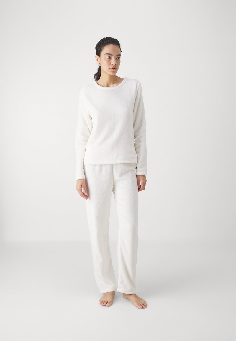 Vit fleece loungemössa set som innehåller en långärmad topp med rundad halsringning och matchande byxor med avslappnad passform och mjuk textur.