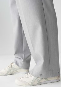 Light gray tailored trousers made of smooth fabric with a subtle texture. Paired with beige sneakers featuring green accents and white soles.