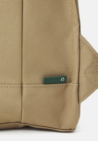Beige fabric bag with a textured surface, featuring a green recycled label, and reinforced stitching at the seams.