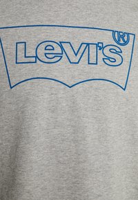 Tissu gris avec le logo Levi's en contour bleu centré dessus, présentant la forme distinctive et le symbole de marque déposée.