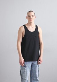 Black sleeveless tank top with a textured logo; paired with light blue cargo pants featuring multiple pockets and a loose fit.