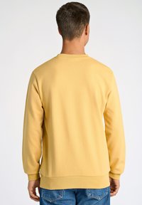 Felpa gialla con maniche lunghe, collo a giro e polsini a costine. Texture liscia, senza motivi visibili, abbinata a jeans denim blu.