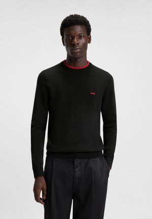 Maglione nero con colletto rosso a coste, dotato di un piccolo logo rosso "HUGO" sul petto. Il materiale appare liscio con un design aderente.