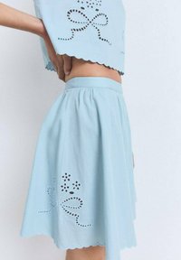 Conjunto de dos piezas de algodón azul claro que incluye una blusa corta con bordes en forma de ola y diseños florales de ojal, combinado con una falda acampanada.