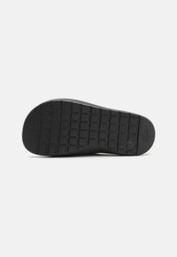 Semelle de chaussure en caoutchouc noir avec un motif de grille texturé, comportant une empreinte de logo et un bord avant légèrement arrondi.