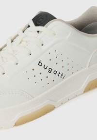 Sneaker alb Bugatti cu panou lateral perforat, șireturile crem, logo-ul negru pe limbă și gulerul interior bej căptușit.