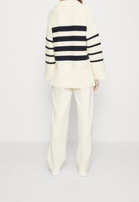 Weißer Strickpullover mit dunkelblauen Horizontalstreifen, weiten Ärmeln und lockerer Passform, kombiniert mit cremefarbenen weit geschnittenen Hosen.