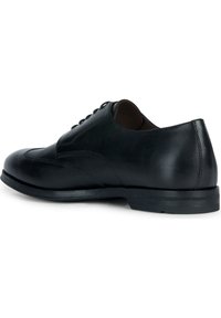Chaussure habillée en cuir noir avec une finition lisse, un design à lacets, des coutures détaillées et une semelle en caoutchouc à profil bas.