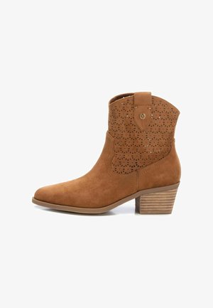 Bota de tobillo de ante marrón con punta afilada, patrón recortado en la parte superior y tacón apilado. Pequeña lengüeta en la parte trasera para facilitar el calzado.