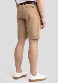 Beige Baumwollkurze Hosen mit geradem Schnitt, seitlichen und hinteren Taschen, einem braunen Gürtel und getragen mit weißen Sneakers. Schlichtes Design und klare Linien.