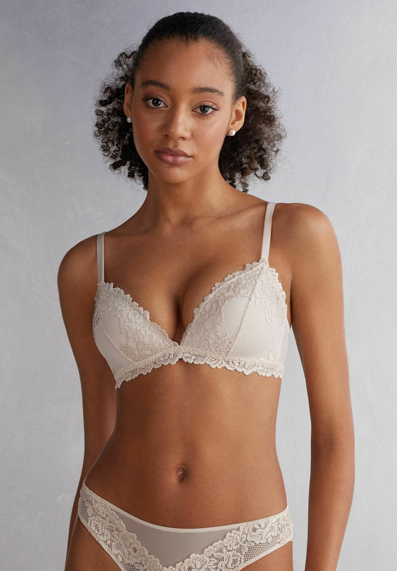 Béžová krajková podprsenka s texturovaným vzorem, s hlubokým výstřihem a nastavitelnými ramínky, doplněná o odpovídající krajkové tanga.