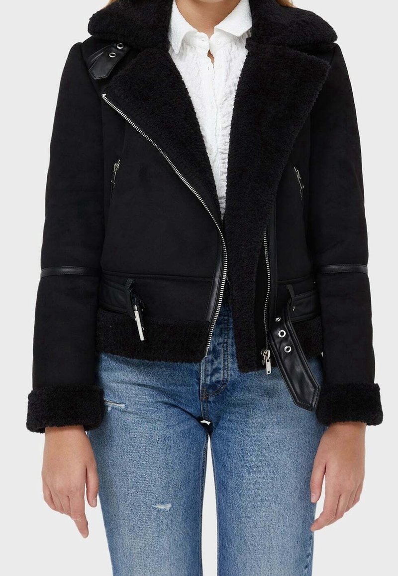Sort faux shearling jakke med læderdetaljer, lynlås-lukning og sidelommer. Har en bred krave og teksturerede ærmekanter.