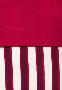 Nahaufnahme einer roten Stoffnaht über einem vertikal rot-weißen gestreiften Strickstoff.