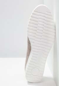 Baskets en daim avec une semelle en caoutchouc blanche plate. La semelle présente des motifs de traction nervurés et un logo circulaire. La couleur est beige clair.