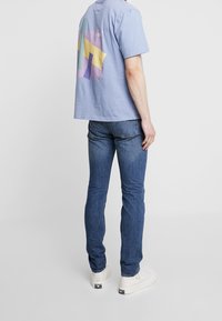 Ljusblå bomull t-shirt med en flerfärgad geometrisk design på baksidan, matchad med mörkblå jeans och vita sneakers.