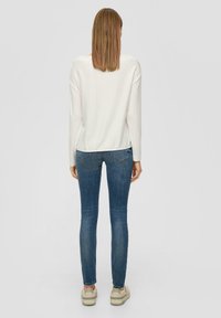 Witte top met lange mouwen en een ronde hals, gecombineerd met slim-fit blauwe jeans. Gestructureerde stof, minimalistisch ontwerp en een casual stijl.