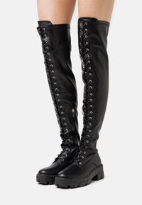Czarne skórzane kozaki sięgające do kolan z detalami w postaci sznurowania i metalowymi oczkami. Masywna platforma i zamek błyskawiczny ułatwiający zakładanie.